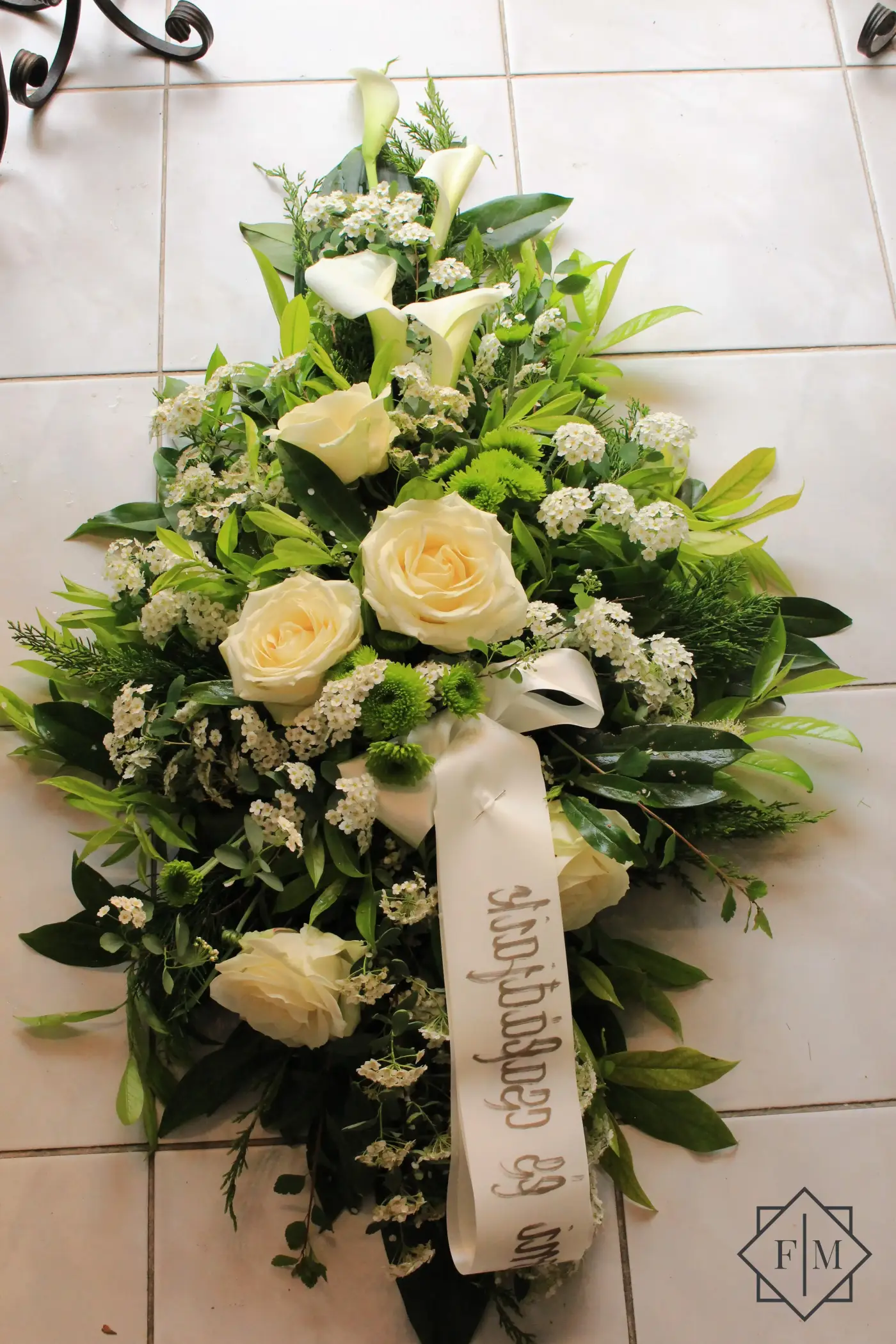 Klasszikus kialakítású sírcsokor krém és fehér színű virágokkal, örök zöldekkel és vízutánpótlással növényeknek. A búcsú személyesebbé tehető, ha kegyeleti csokorba kéred elhunyt kedvenc virágait.