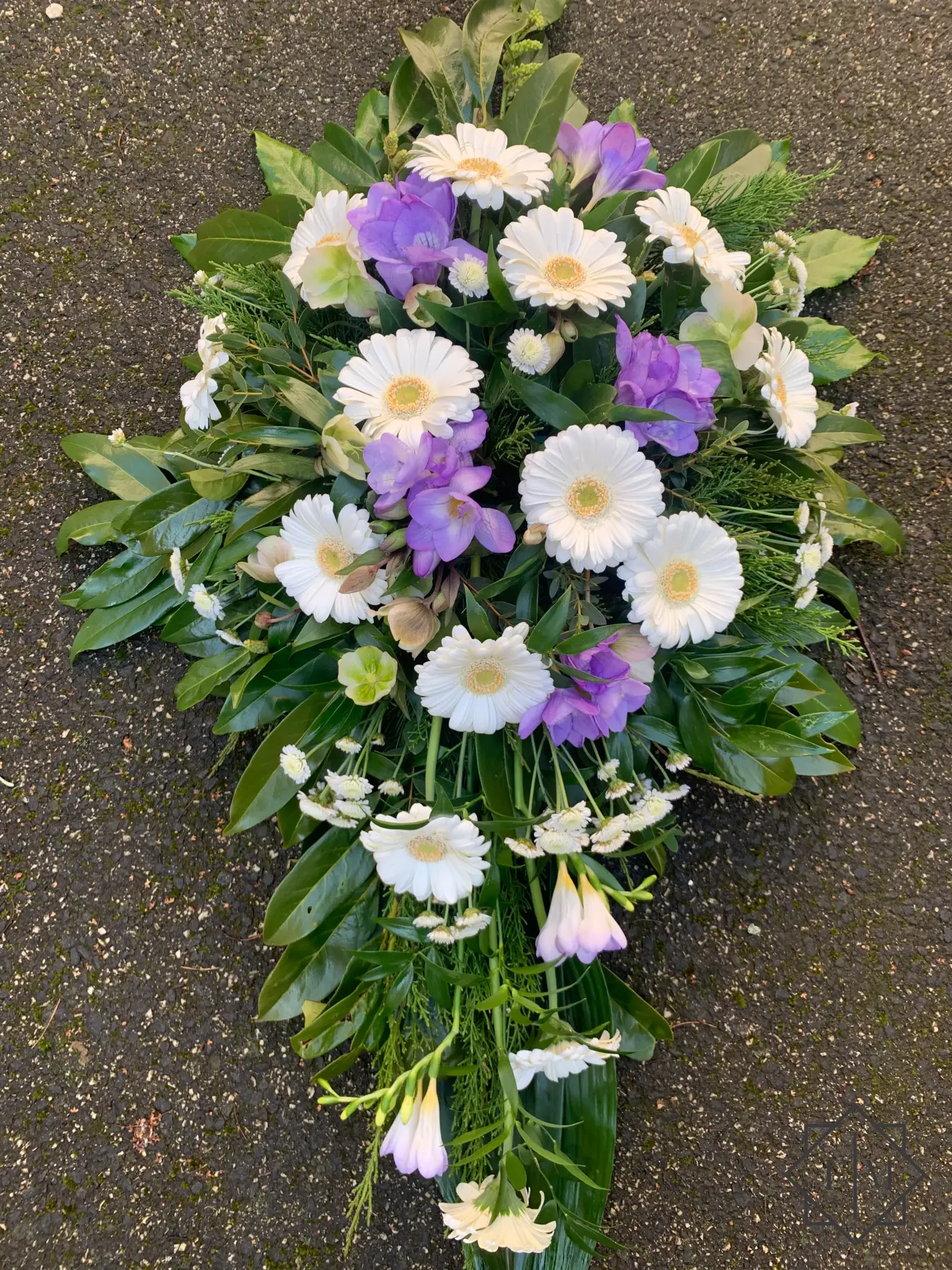 Klasszikus kialakítású sírcsokor lila és fehér színű virágokkal, örök zöldekkel és vízutánpótlással növényeknek. A búcsú személyesebbé tehető, ha kegyeleti csokorba kéred elhunyt kedvenc virágait.